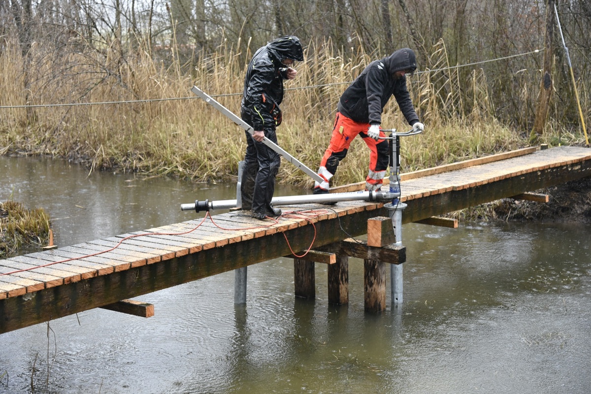 Arbeiter schrauben die Stahlpfosten für den Steg ins Wasser