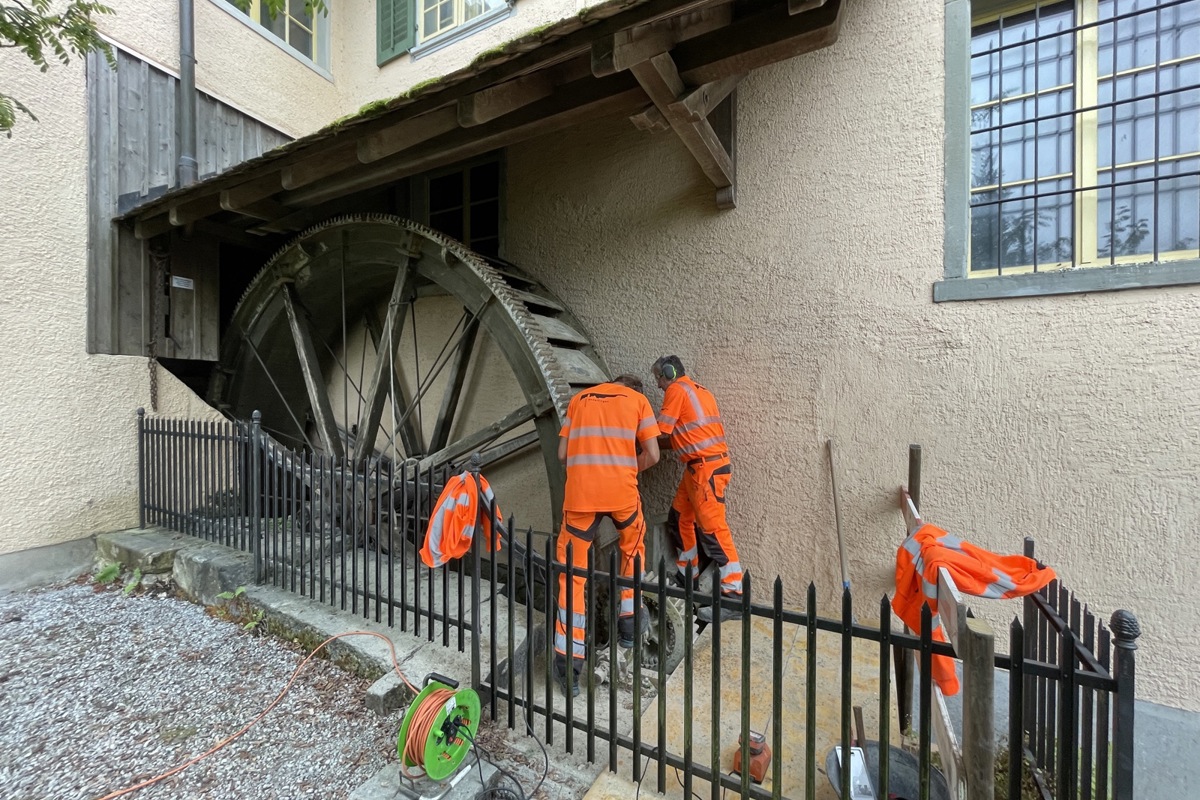 Kalkablagerungen unerwünscht: Der Zahnkranz auf der Vorderseite des Mühlrads muss sauber ins kleinere Ritzel (zu Füssen der Arbeiter) greifen können.