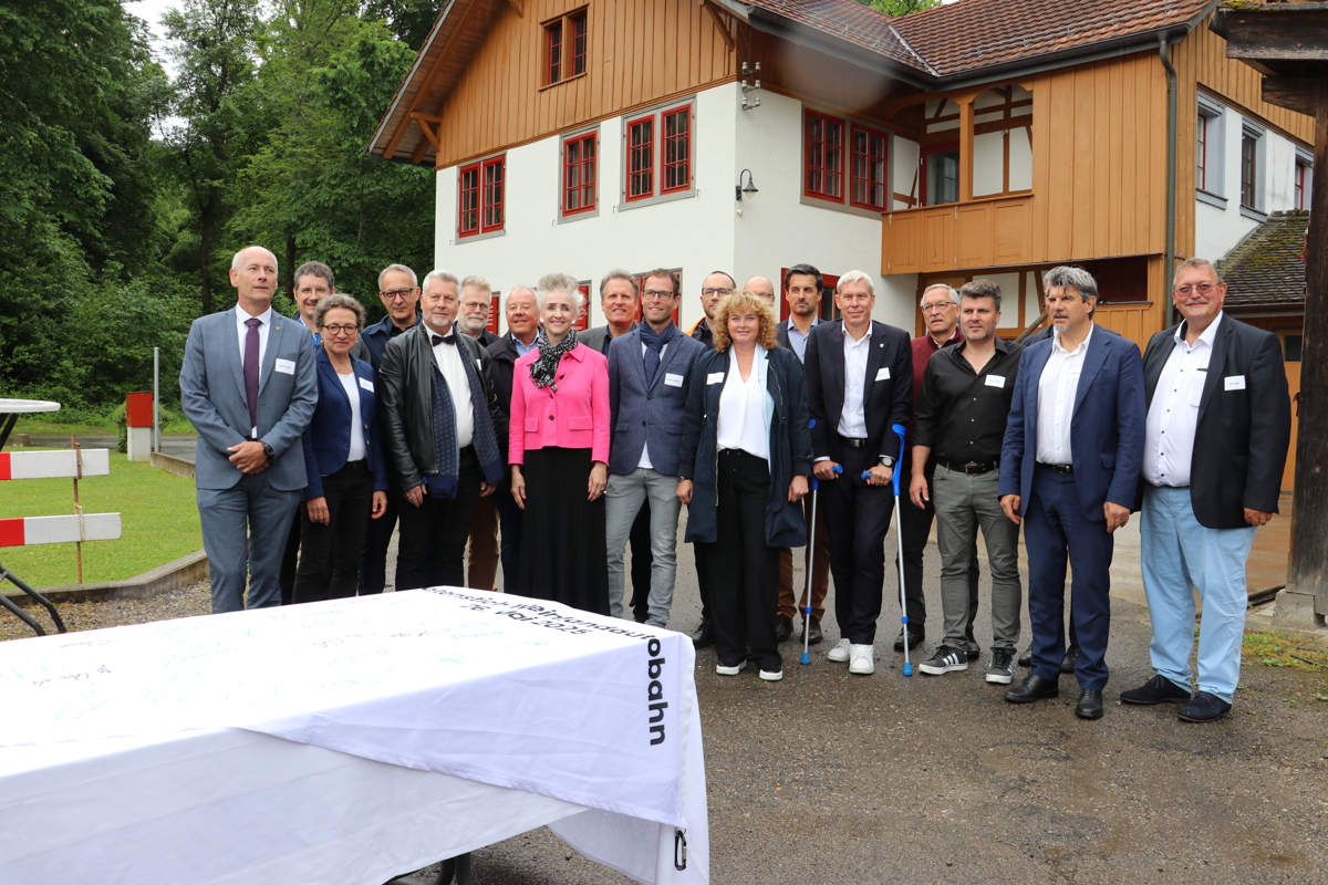 Die Zürcher Regierungsrätin Carmen Walker Späh (Mitte), Astra-Vizedirektor Guido Biaggio (rechts) und Schaffhausens Regierungsratspräsident Martin Kessler (links) sowie Vertreterinnen und Vertreter der betroffenen Gemeinden haben den Wimpel (vorne) unterschrieben, der dann unter der Autobahnbrücke aufgehängt wurde.