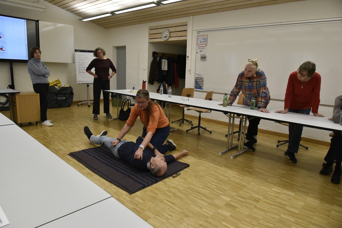 Samariterlehrerin Heidi Strasser (oranger Pullover) zeigt, wie ein Patient in die stabile Seitenlage gebracht wird.