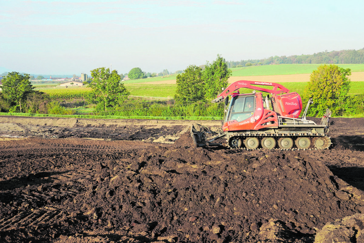 Dank Seilwinde und breiten Raupen ist der Pistenbully bodenschonend unterwegs. Die dunkle Erde ist Torf